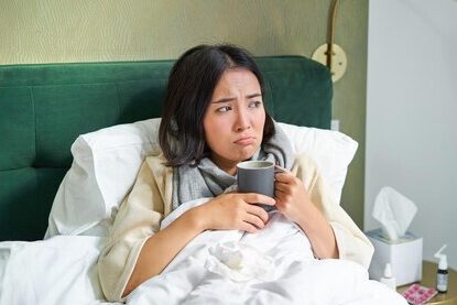 woman feeling bloated, sick, and tired, in bed with a hot cup of tea