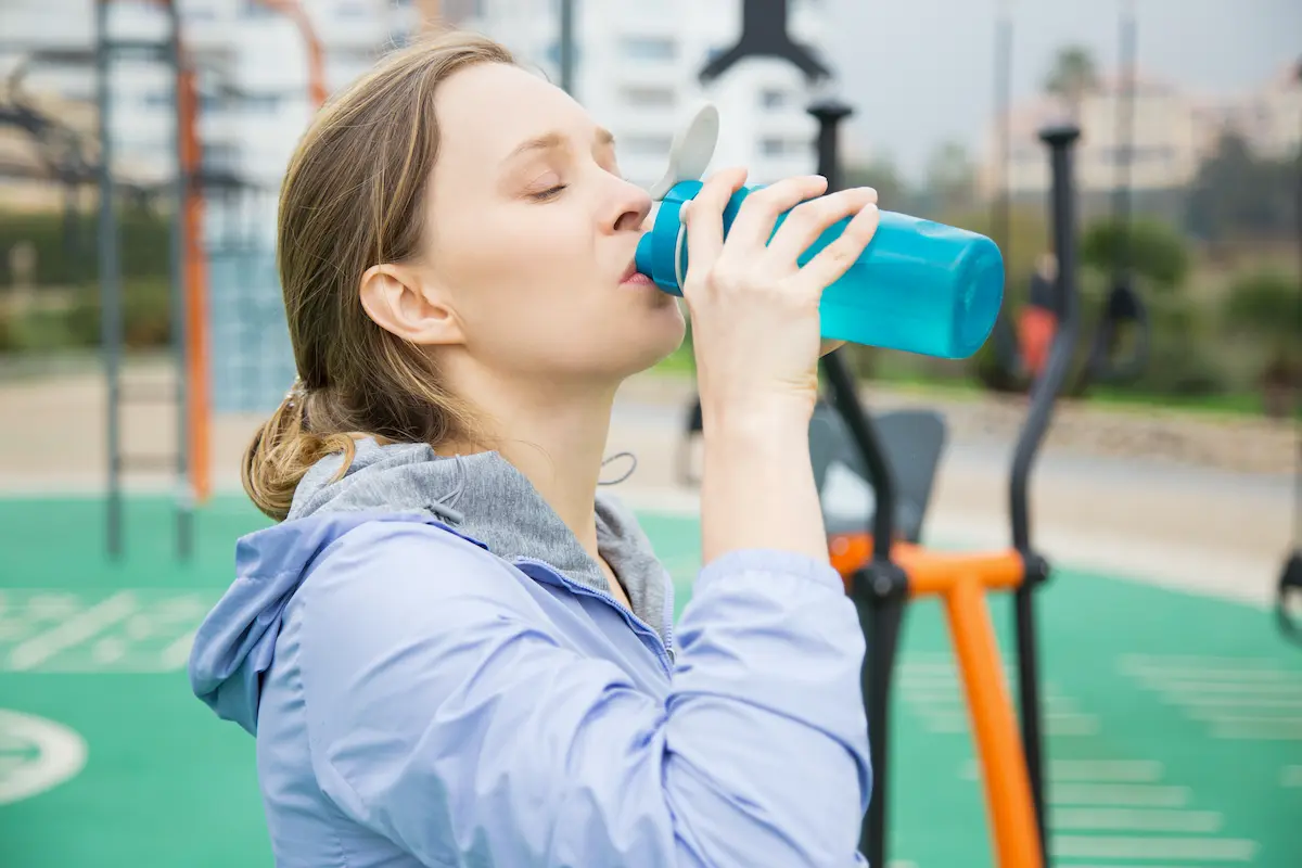 a woman drinking too many electrolytes from a blue bottle